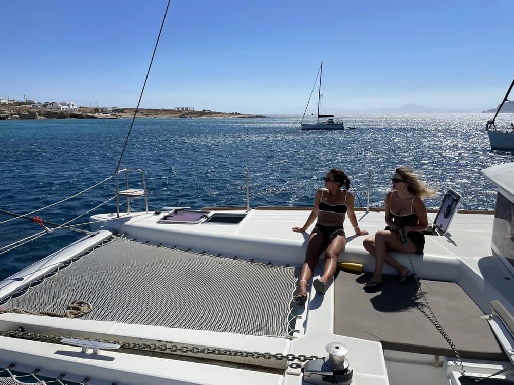 view of two girls on a sailing catamaran in the Cyclades