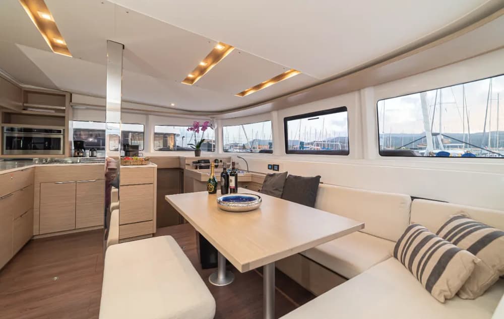 Lagoon 46 interior saloon featuring a spacious dining area, modern galley, and panoramic windows, offering comfort and luxury for a catamaran sailing holiday.