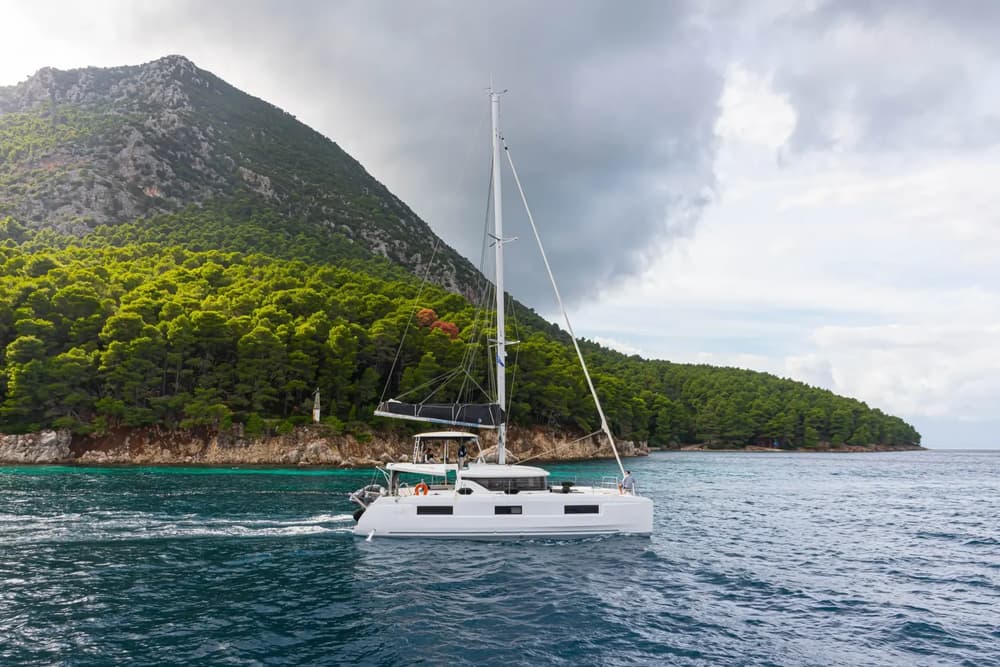 Lagoon 46 sailing catamaran cruising along a lush green coastline, showcasing its sleek design and spacious deck layout for an unforgettable yacht charter experience.