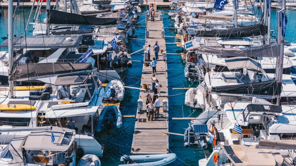 A busy Mediterranean marina with catamarans and sailing yachts during a yacht charter meetup, highlighting fleet inspection and broker-client networking on the dock.