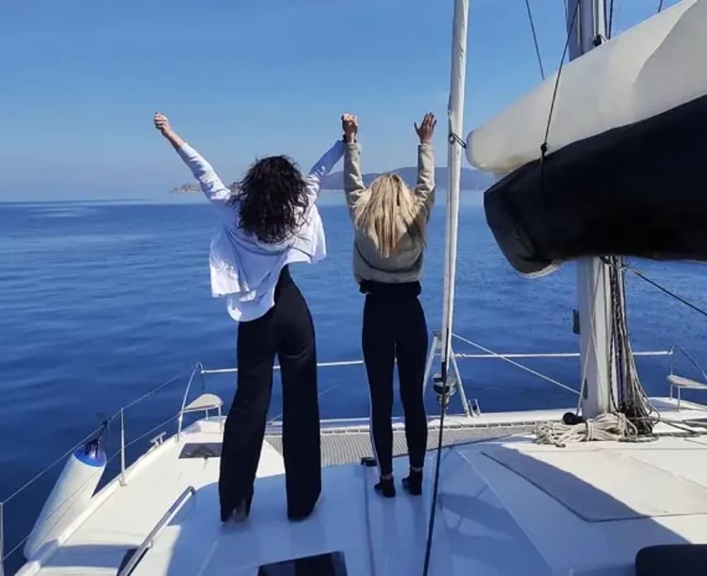 Two friends standing on a sailboat deck, celebrating the perfect sailing holiday in Athens, Greece.