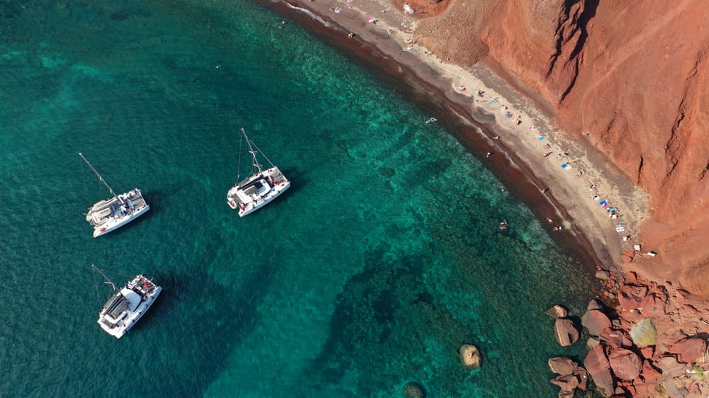 Aerial view of catamarans anchored in turquoise waters near a secluded beach, ideal for a bareboat charter adventure.