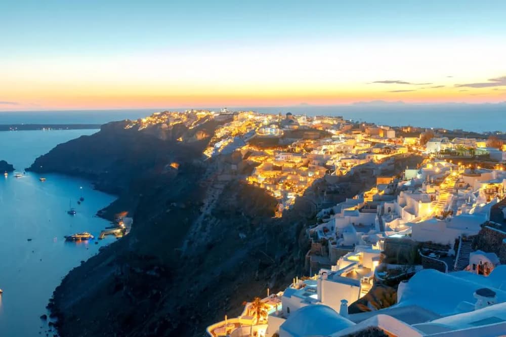 Santorini's famous whitewashed buildings illuminated at sunset, a premier luxury sailing destination frequented by celebrities in Greece.