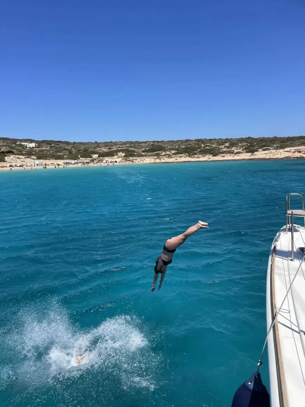 girl jumping off a boat in crystal clear turquoise water in the Cyclades islands