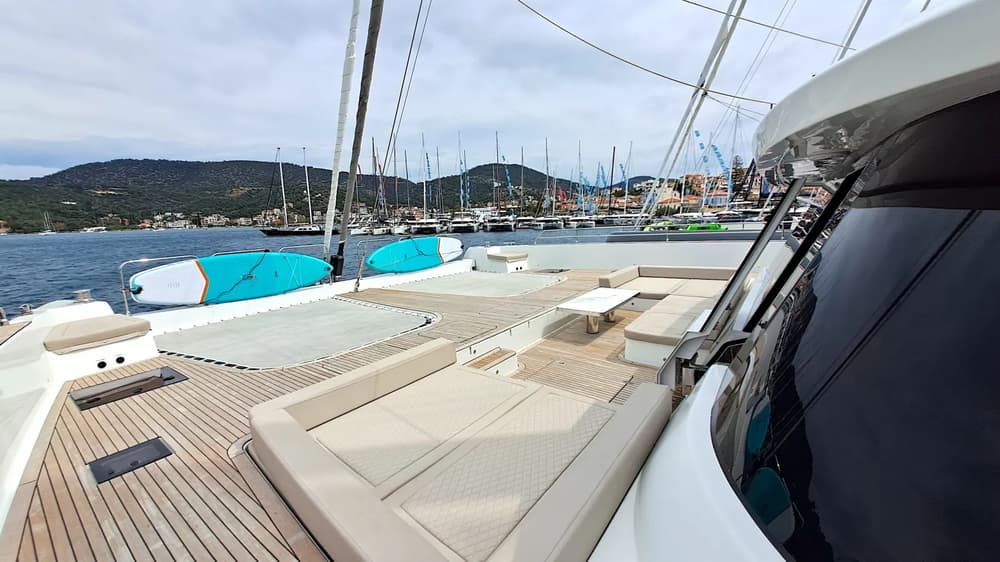Spacious sunbathing area on a fully crewed catamaran with scenic marina views, featuring paddleboards and plush seating for a luxurious yacht charter experience.