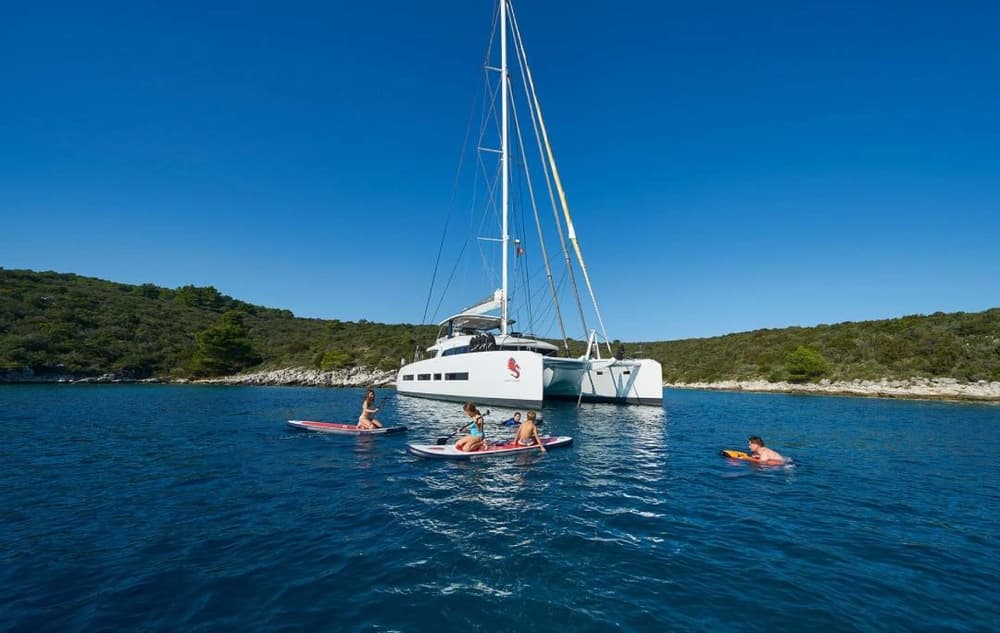 Guests enjoying water activities such as paddleboarding and swimming around the Lagoon 77, highlighting the yacht’s ideal setup for fun-filled sailing adventures.
