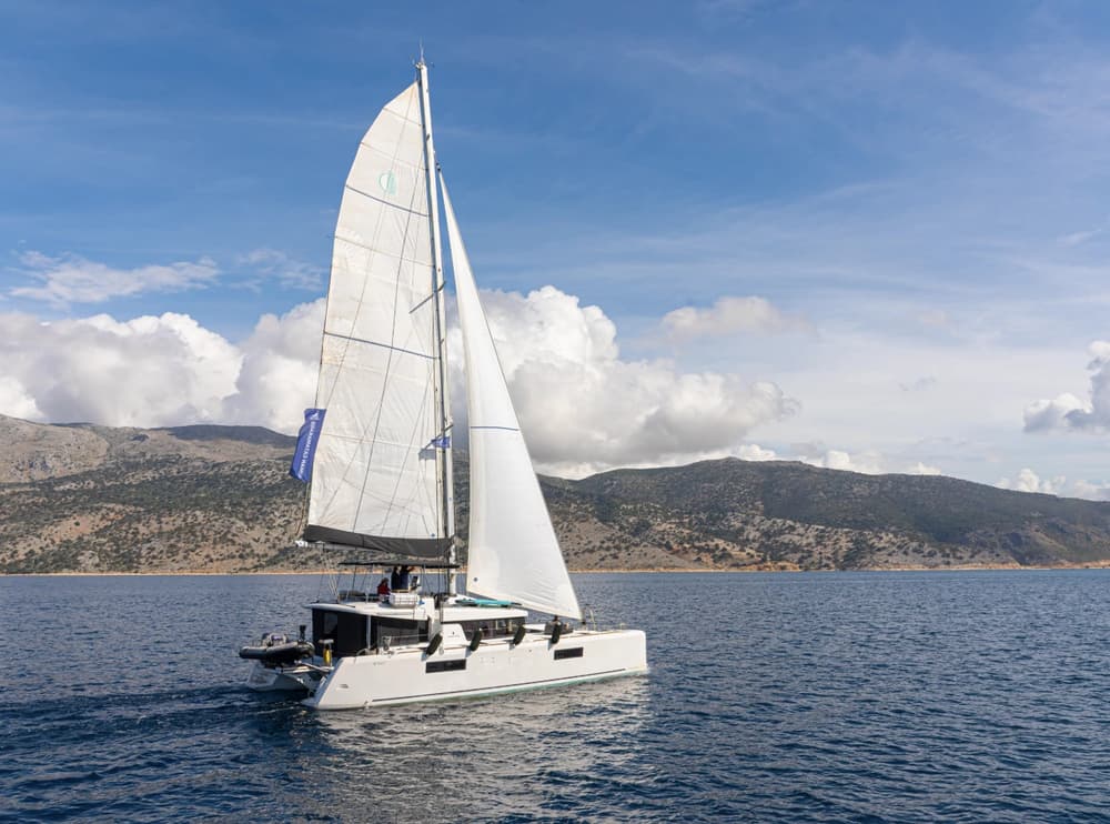 Lagoon catamaran sailing in open waters with mountainous scenery, highlighting its sleek design and smooth sailing performance.