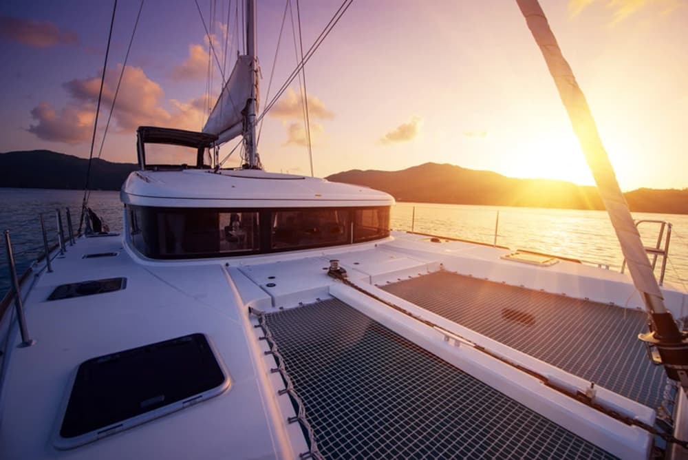 Luxury catamaran's forward deck with trampolines and sunbeds at sunset, offering a relaxing space for sailing holidays.