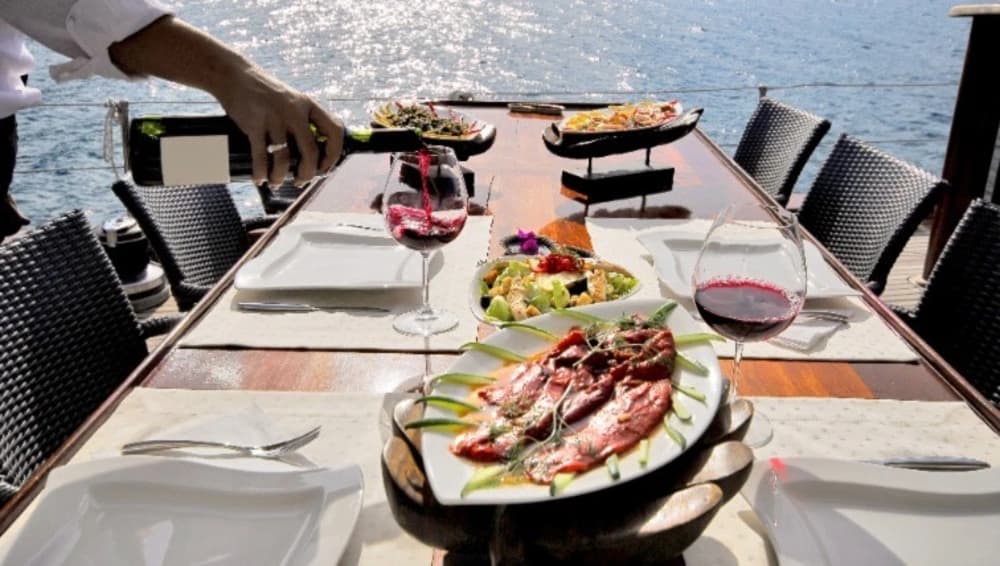A gourmet meal with wine served on the deck of a luxury yacht, showcasing the fine dining experience provided during a fully crewed yacht charter