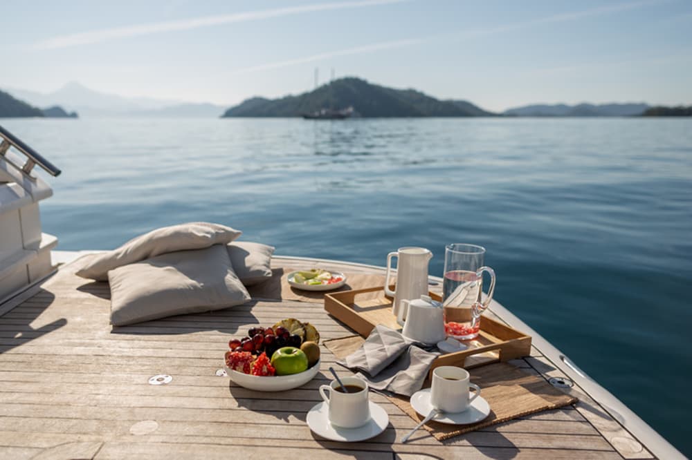 A gourmet breakfast served on the deck of a yacht, with calm waters and scenic islands in the background, representing the indulgence of a fully crewed charter experience.