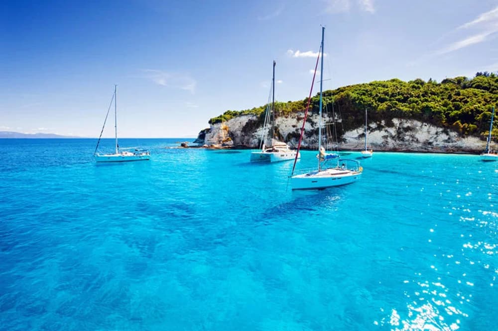 Sailing holidays in Corfu – anchored sailing yachts in crystal-clear turquoise waters near lush green islands. Ideal for Corfu yacht charters, Ionian sailing routes, and Greece sailing itineraries.