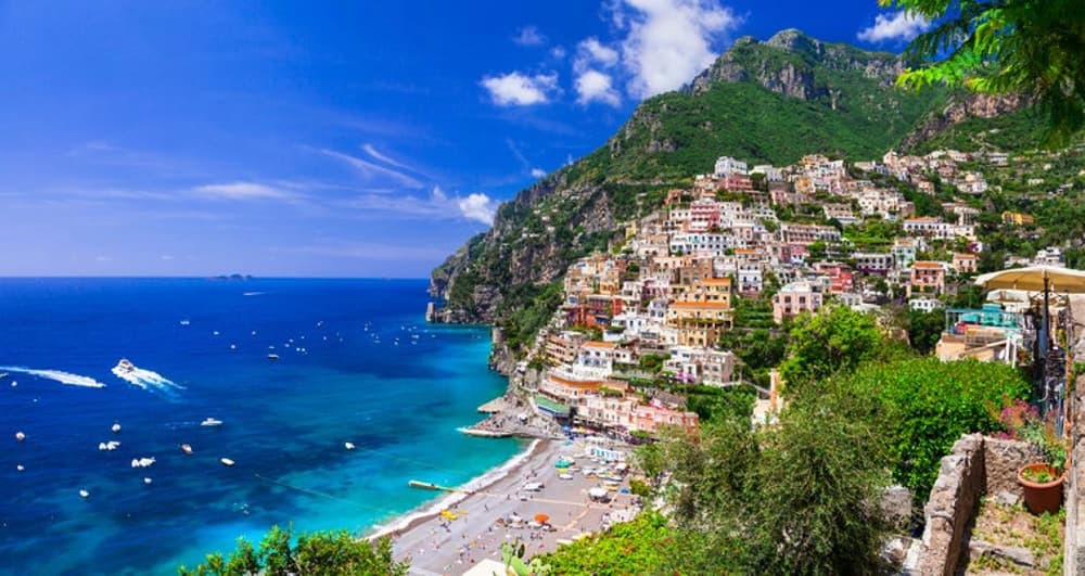 The picturesque Amalfi Coast featuring colourful cliffside houses and serene blue waters – a highlight of sailing holidays in Italy.