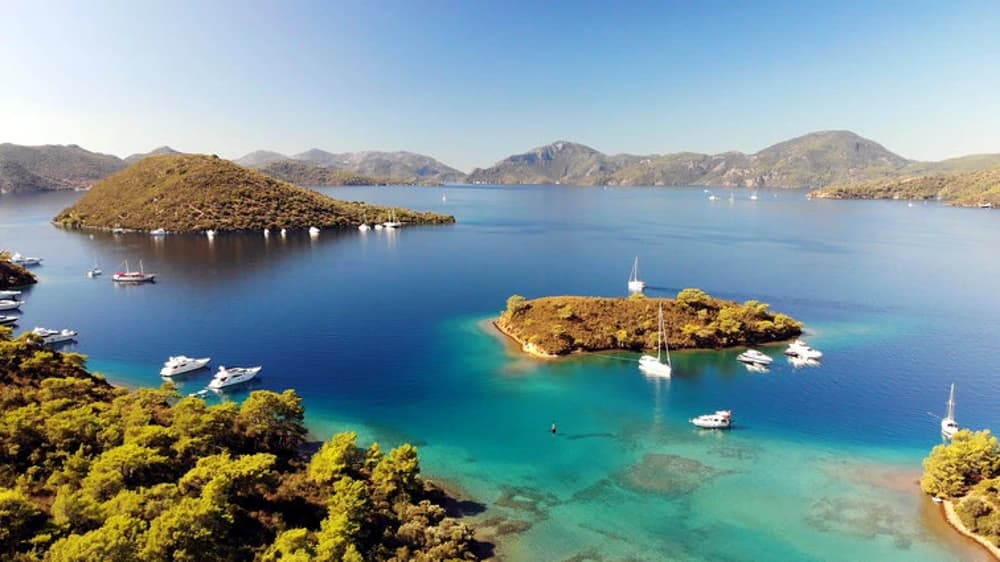 Aerial view of Fethiye Gulf in Turkey, showcasing calm turquoise waters, lush green islands, and moored yachts, a popular destination for yacht charters and sailing holidays on the Turquoise Coast