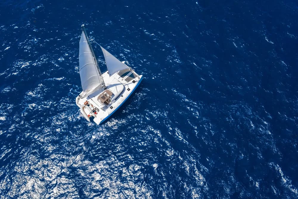 sailing catamaran with open sails on charter in blue water