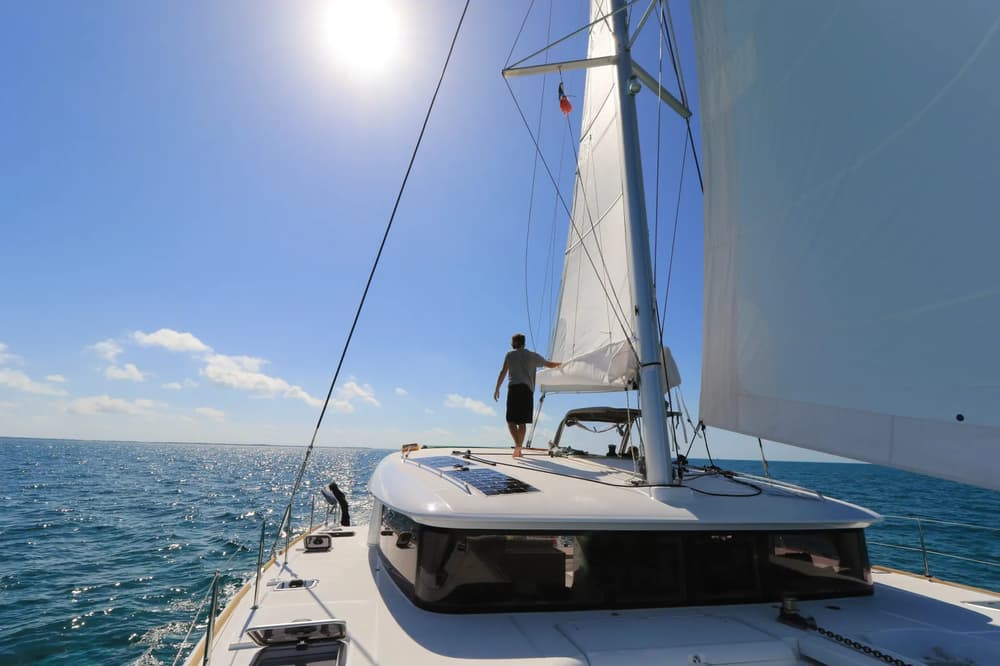 A skipper standing at the bow of a catamaran, adjusting the sails under the bright sun, highlighting the thrill of a skippered sailing holiday.
