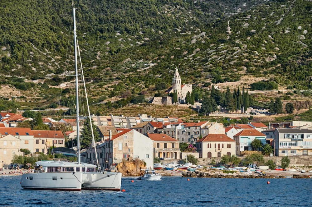 A modern catamaran moored off the coast of a charming Mediterranean town, offering the perfect setting for a skippered yacht charter getaway.