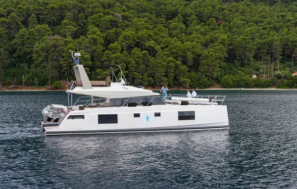 Luxury power catamaran charter anchored in peaceful Mediterranean bay with forested coastline during late-season sailing
