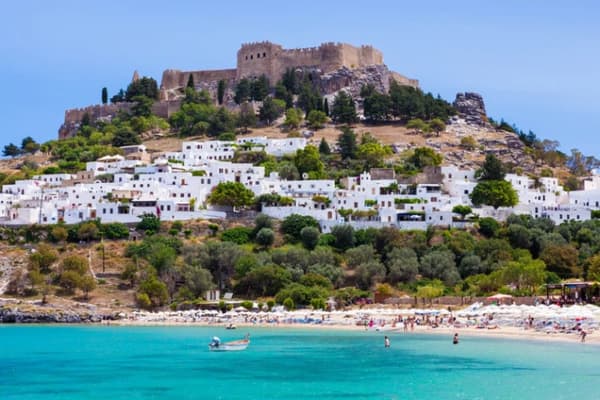 Stunning view of Lindos in Rhodes, showcasing the Acropolis above white-washed houses and turquoise waters, a top stop for sailing holidays in the Dodecanese.