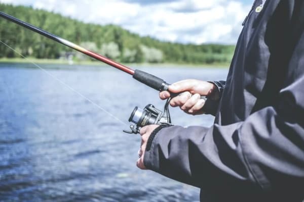 Close-up of an angler holding a fishing rod while sailing, showcasing a serene lake and forest background.