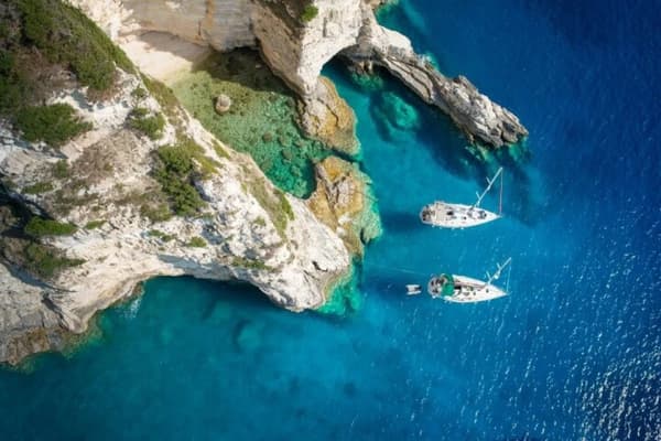 Two sailing yachts anchored in a secluded cove with crystal-clear waters in the Mediterranean, showcasing affordable yacht charter options for budget-friendly sailing holidays with Yacht4Less.