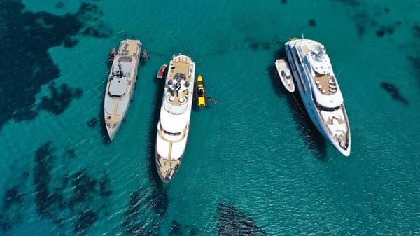 Three luxurious yachts anchored in crystal-clear turquoise waters, with small boats and water toys nearby, showcasing the premium experience of fully crewed yacht charters.