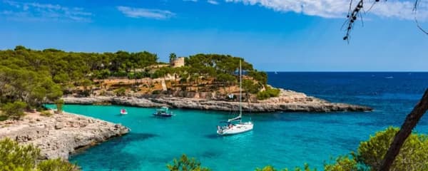 Sailing yacht anchored in a secluded cove in Mallorca, Spain, surrounded by crystal-clear turquoise waters and lush Mediterranean landscape – ideal for a Mallorca sailing holiday.