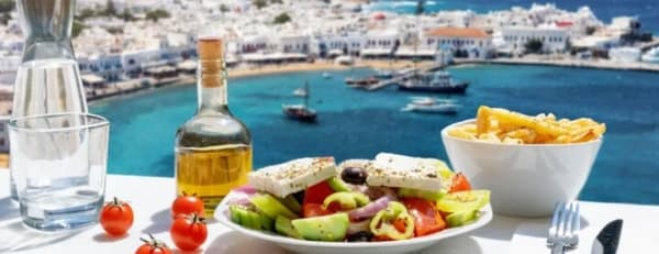 Traditional Mediterranean cuisine by the sea – Greek salad, olive oil, and fresh ingredients with a yacht-filled harbour in the background.