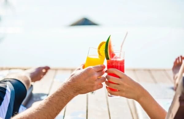Couple enjoying refreshing cocktails on a romantic sailing holiday, set against a serene sea backdrop.