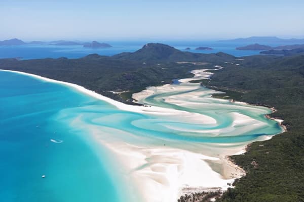 An aerial view of Whitehaven Beach in the Whitsundays, featuring turquoise waters, white sandy shores, and lush greenery, showcasing the breathtaking beauty of sailing holidays in Australia.