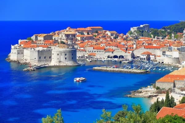 A breathtaking view of Dubrovnik's Old Town with its iconic red-roofed buildings, historic walls, and a vibrant marina, showcasing the charm of sailing holidays in Croatia.