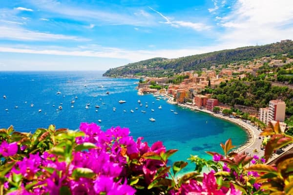 A stunning view of Villefranche-sur-Mer on the French Riviera, with vibrant flowers in the foreground, sailboats in the turquoise bay, and hillside villas, showcasing the elegance of sailing holidays in France.