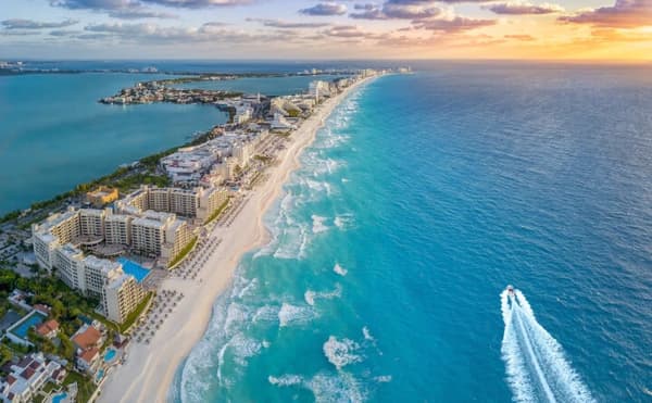 An aerial view of Cancun’s coastline at sunset, featuring white sandy beaches, turquoise waters, and luxury resorts, showcasing the allure of sailing holidays in Mexico.