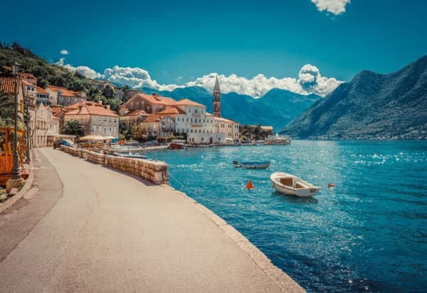 A scenic view of Perast on the Bay of Kotor in Montenegro, with historic buildings, small boats on the sparkling water, and towering mountains in the background, capturing the charm of sailing holidays in Montenegro.