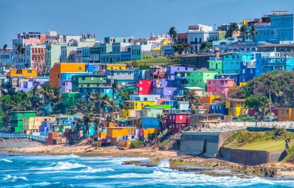 A vibrant view of colourful houses in San Juan, Puerto Rico, overlooking the ocean waves, showcasing the lively culture and scenic beauty of sailing holidays in Puerto Rico.