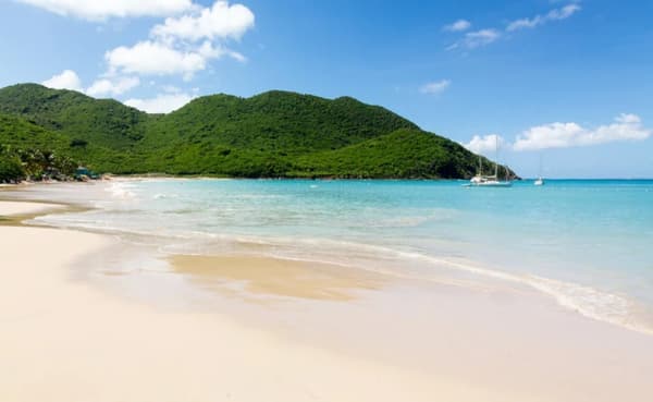 A serene beach in Saint Martin with white sand, clear turquoise waters, and a sailboat in the distance, highlighting the peaceful beauty of sailing holidays in the Caribbean.