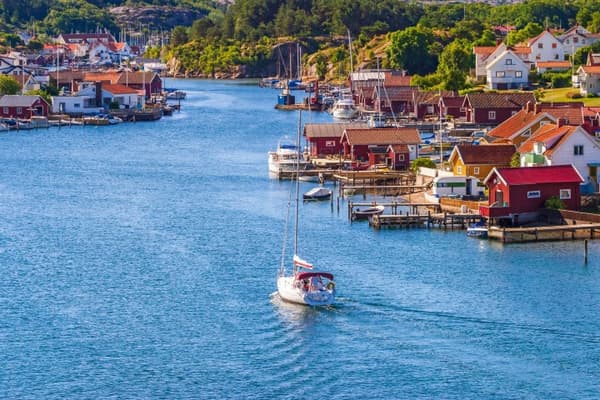 A sailboat cruising through a picturesque Swedish coastal village with colourful houses, calm waters, and scenic harbours, showcasing the charm of sailing holidays in Sweden.