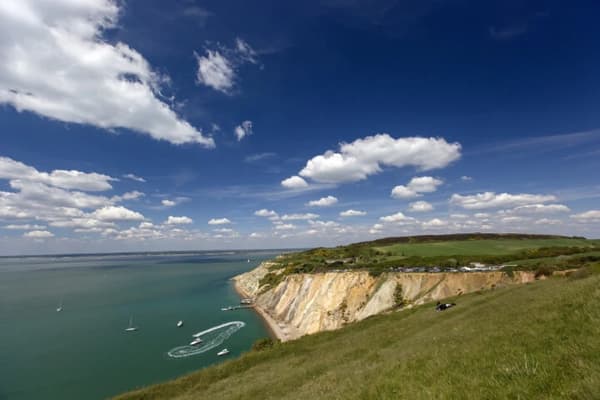 A scenic view of the Isle of Wight coastline with sailing boats in the calm waters below, highlighting the natural beauty of sailing holidays in the United Kingdom.