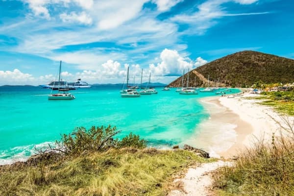A pristine beach in the US Virgin Islands with turquoise waters, anchored sailboats, and lush hills, capturing the tropical allure of sailing holidays in USVI.