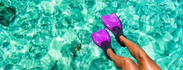 A person wearing purple flippers floating in crystal-clear turquoise waters, showcasing the vibrant marine life and water activities available during a sailing vacation in Florida.