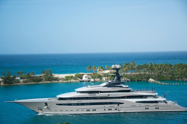 Luxury motor yacht sailing along a tropical coastline with clear blue water and palm trees in the background, perfect for a high-end summer charter.