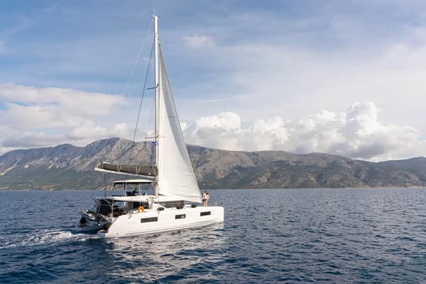 Lagoon 46 catamaran review – Lagoon 46 sailing catamaran gliding across the sea with a stunning mountainous backdrop, showcasing its sleek design and performance for luxury yacht charters.